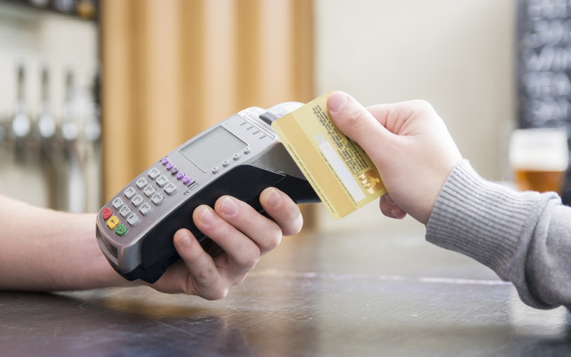 Imagem recortada de uma pessoa pagando com cartão de crédito em uma maquininha de cartão